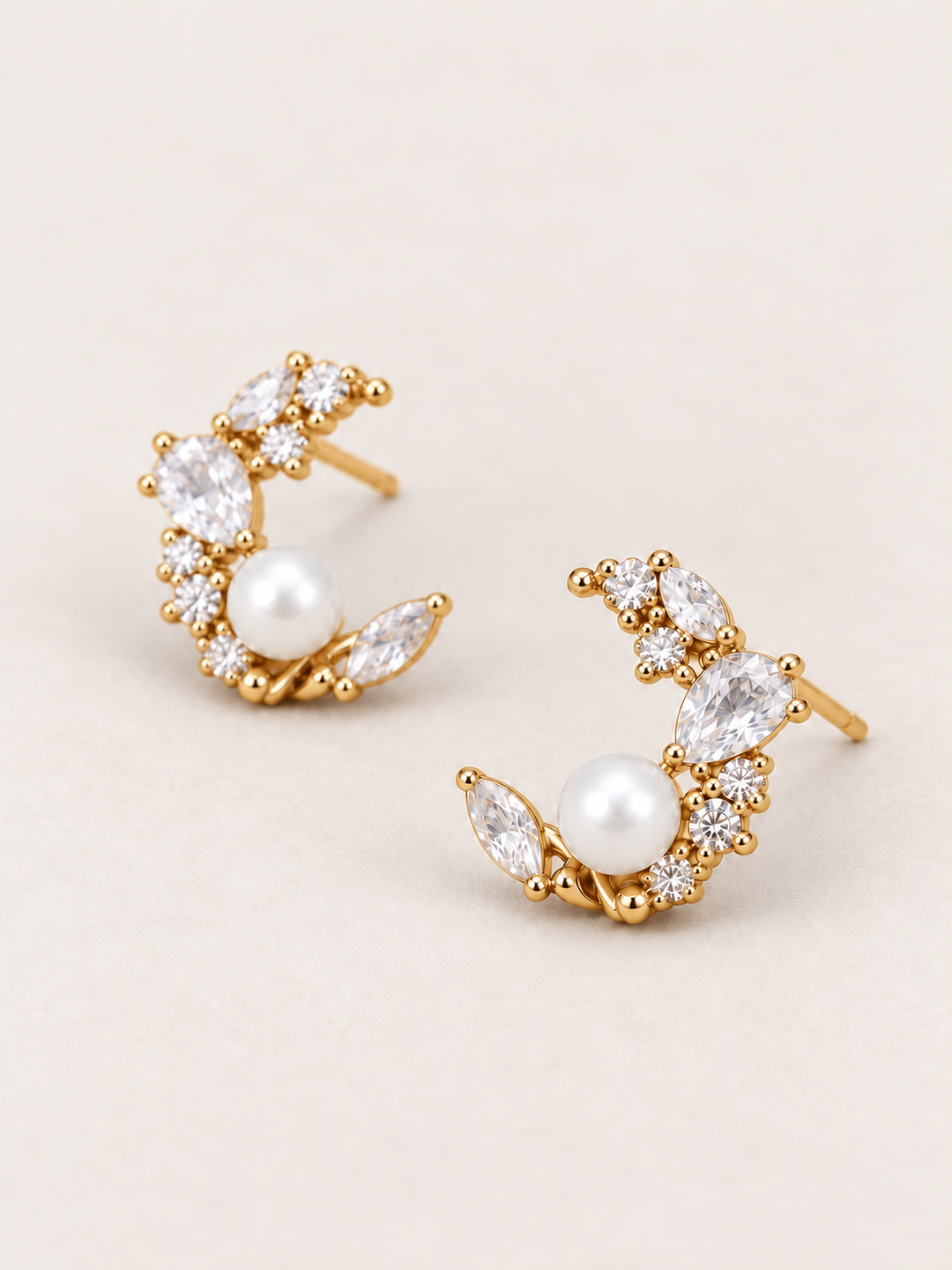 Gold Pearl Crystal Crescent Earrings shown angled on a warm neutral background