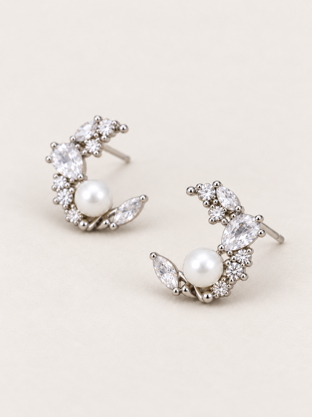 Silver Pearl Crystal Crescent Earrings shown angled on a warm neutral background