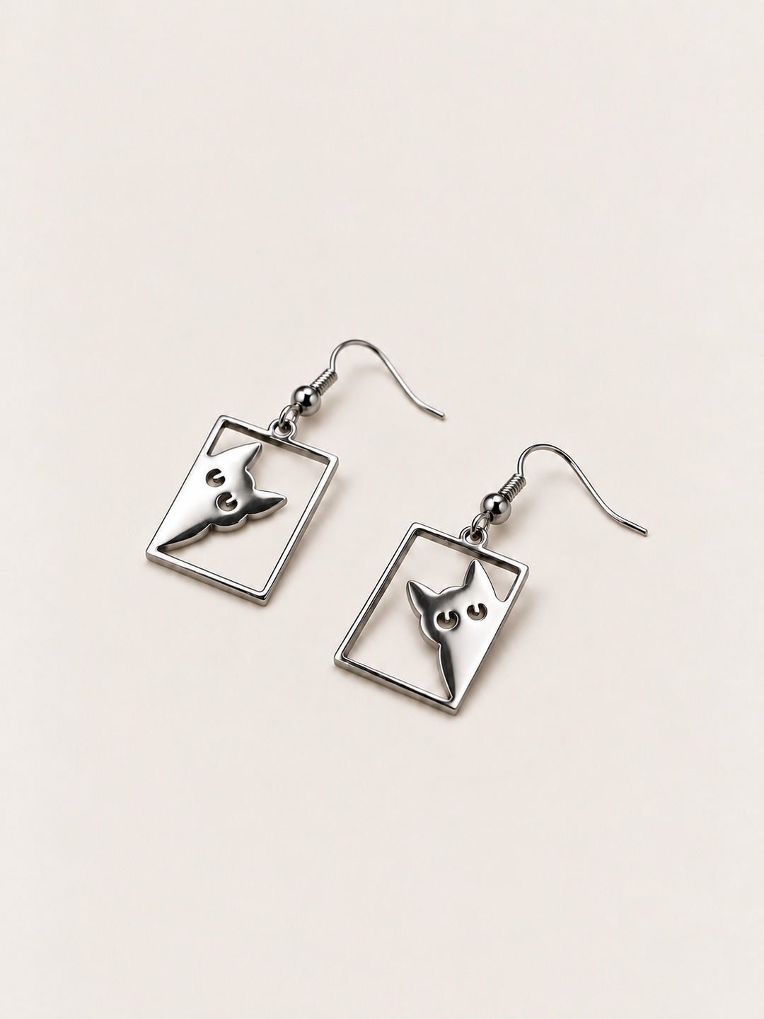 Silver Peeking Cat Rectangle Drop Earrings lying flat at an angle on a warm neutral background