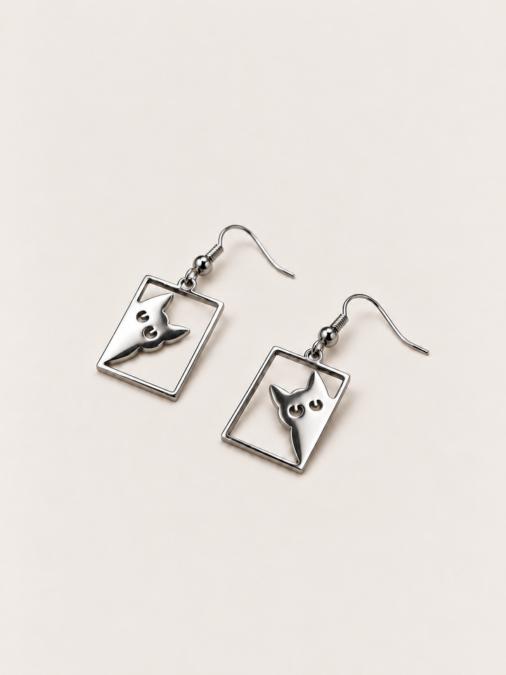 Silver Peeking Cat Rectangle Drop Earrings lying flat at an angle on a warm neutral background