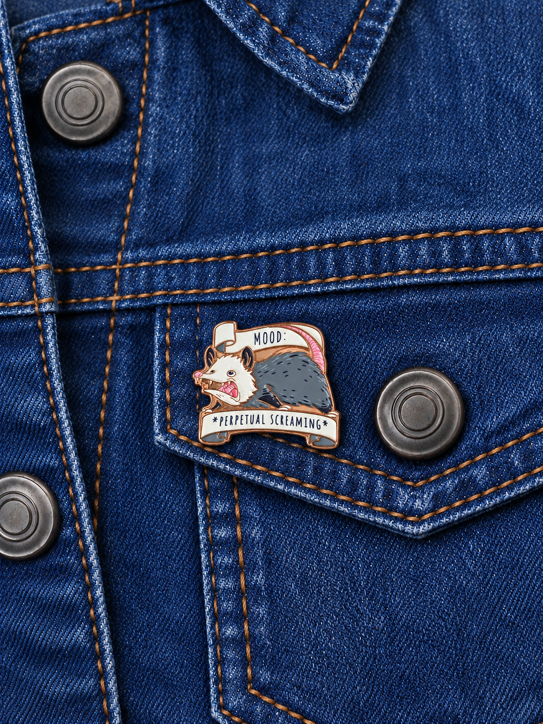 Perpetual Screaming Opossum Pin displayed on a dark indigo denim jacket beside a metal button