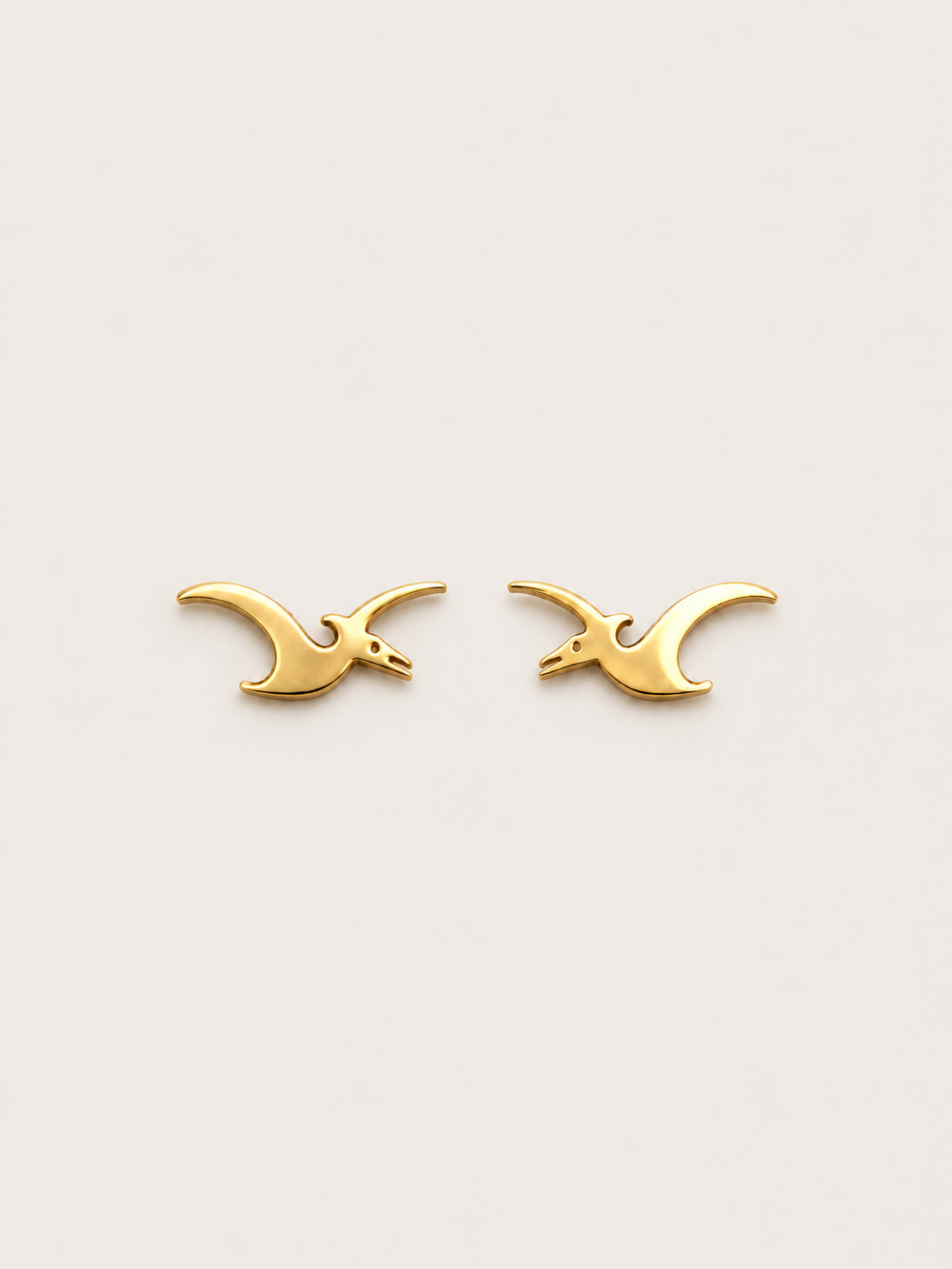 Pterodactyl Stud Earrings in Gold on a warm neutral background