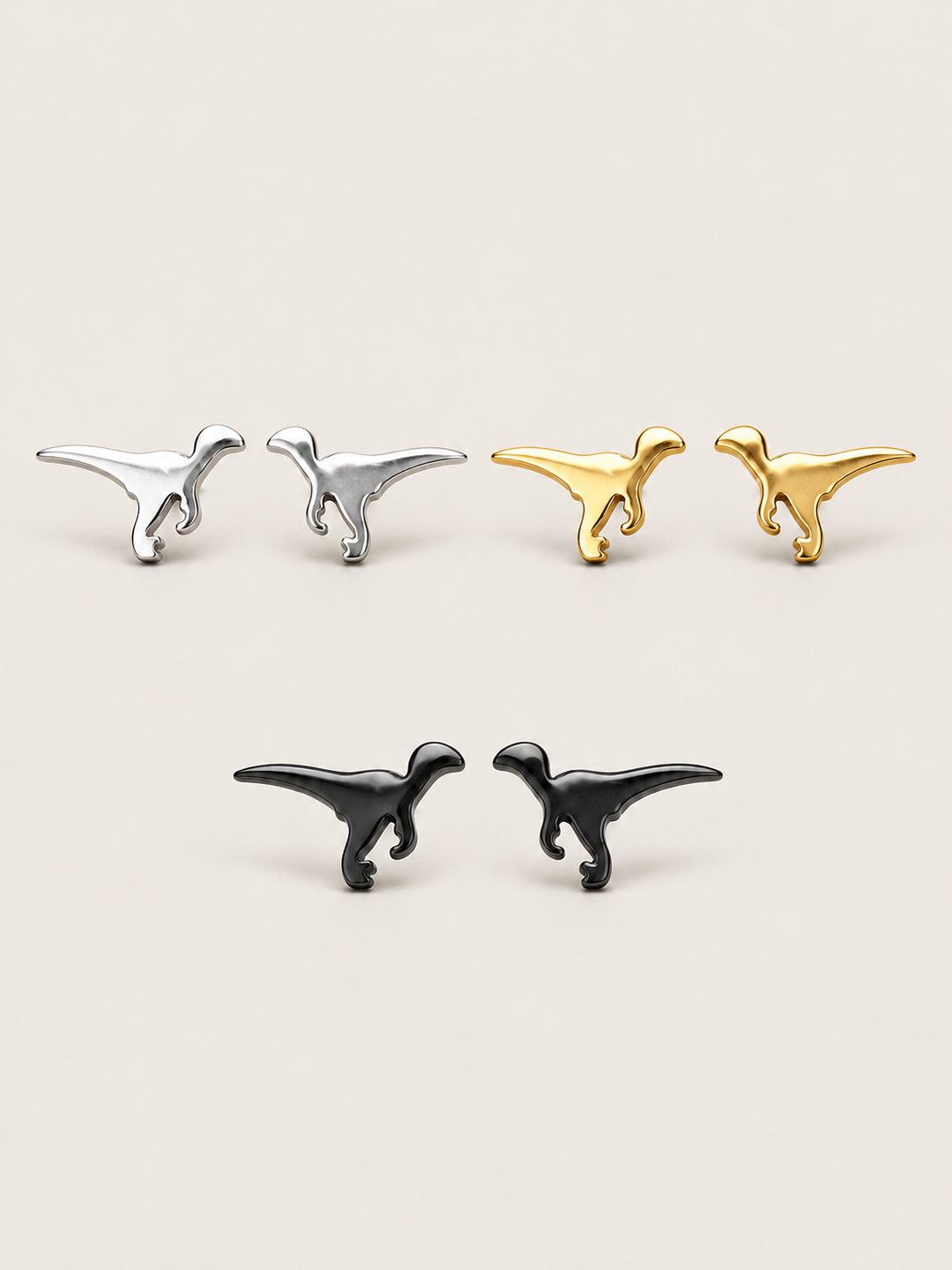 Raptor Dinosaur Stud Earrings in silver, gold, and black on a warm neutral background