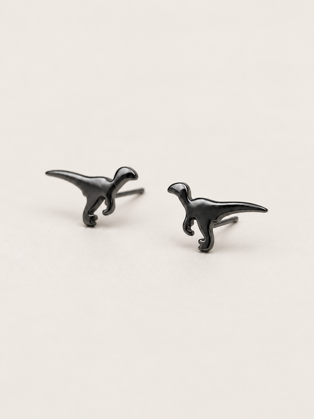 Black Raptor Dinosaur Stud Earrings shown angled on a warm neutral background