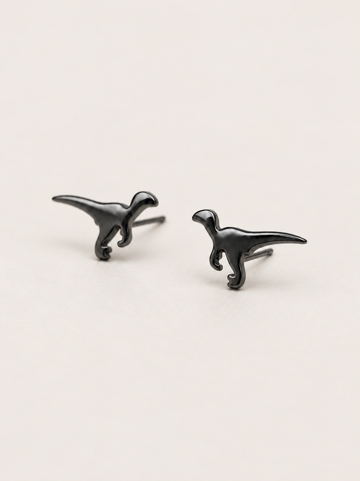 Black Raptor Dinosaur Stud Earrings shown angled on a warm neutral background