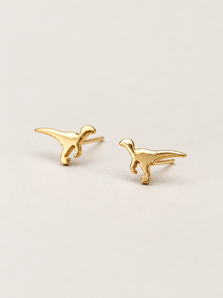 Gold Raptor Dinosaur Stud Earrings shown angled on a warm neutral background