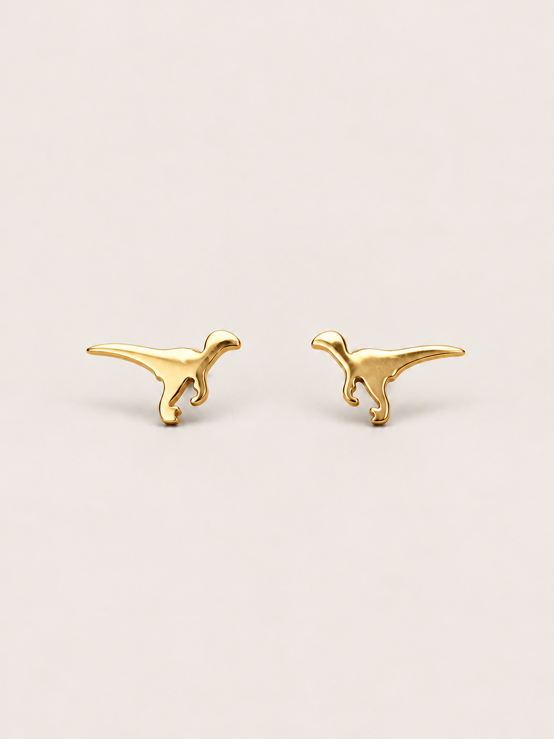 Gold Raptor Dinosaur Stud Earrings shown on a warm neutral background