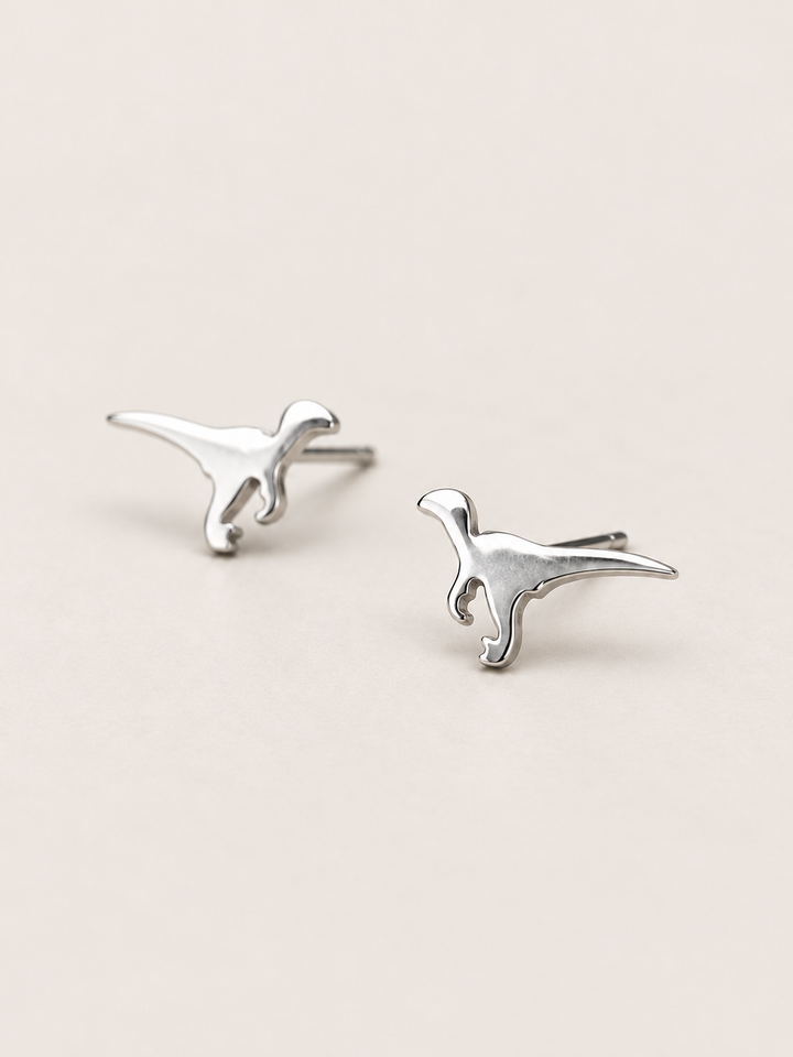 Silver Raptor Dinosaur Stud Earrings shown angled on a warm neutral background
