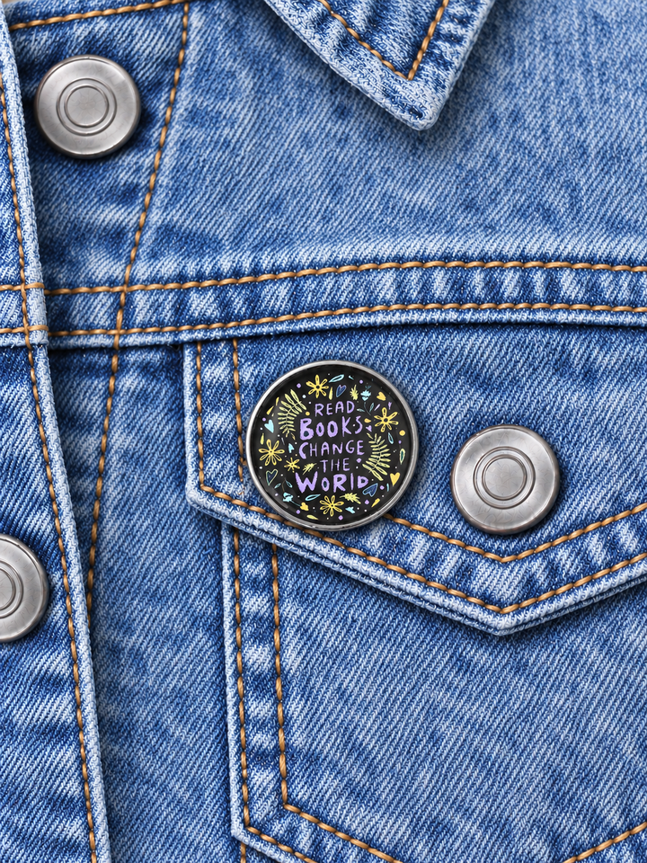 Read Books Change the World Floral Pin displayed on an acid-wash denim jacket beside a metal button