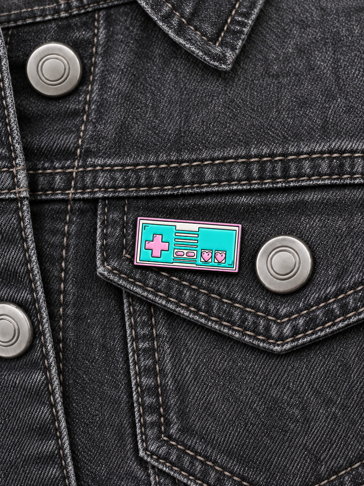 Retro Video Game Controller Pin displayed on a charcoal denim jacket beside a metal button