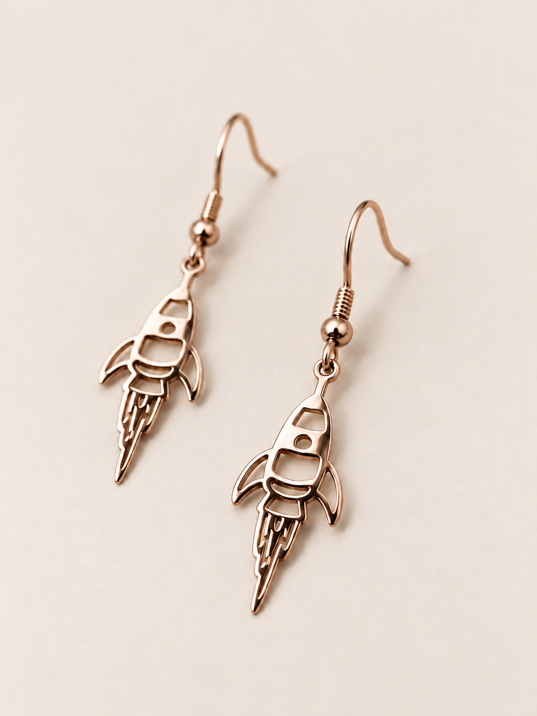 Rose Gold Rocket Drop Earrings shown angled on a warm neutral background