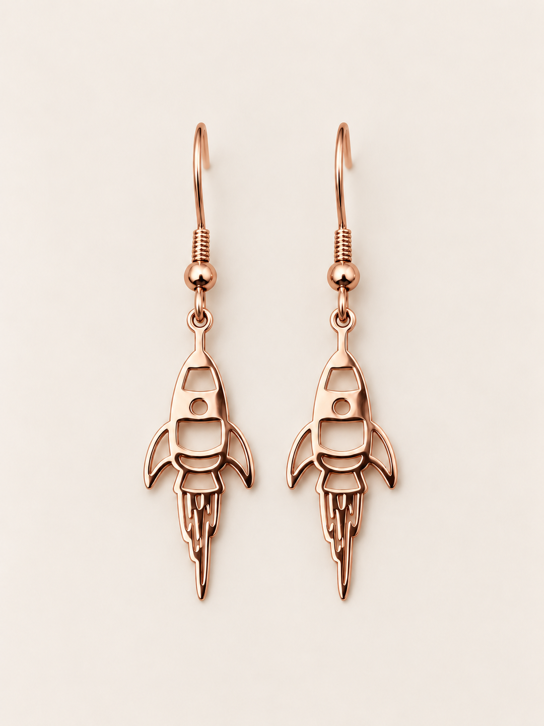 Rose Gold Rocket Drop Earrings on a warm neutral background