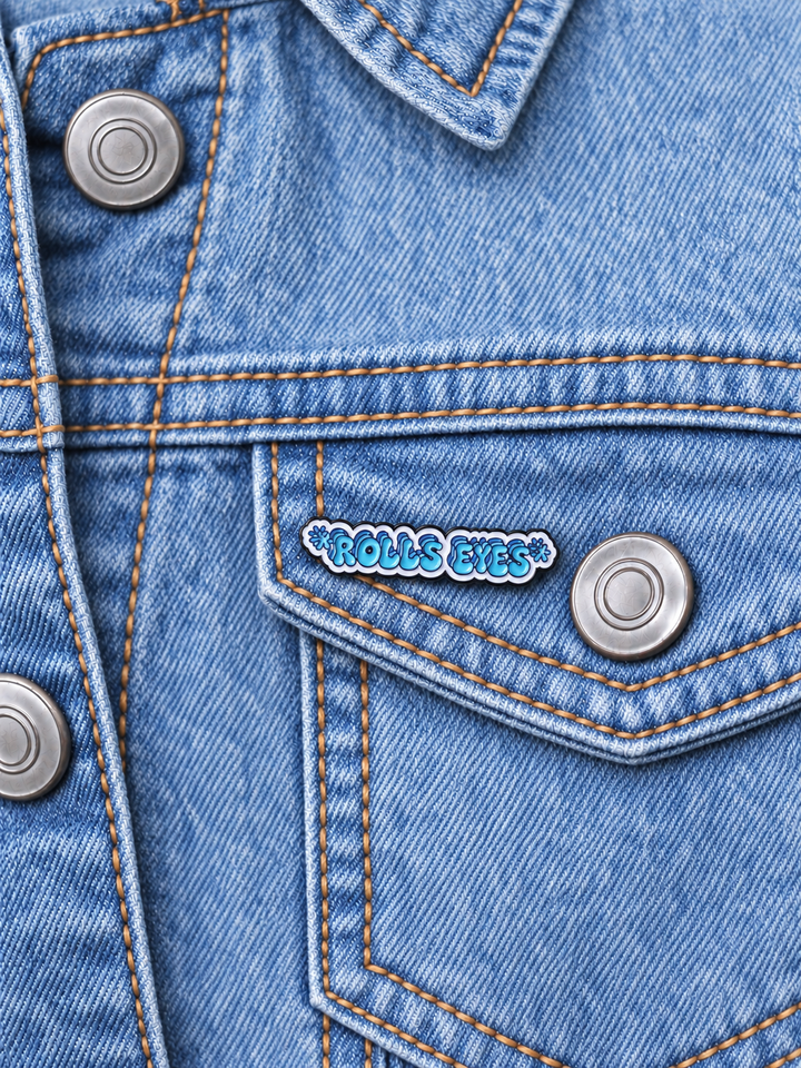 Rolls Eyes Pin displayed on a light-wash denim jacket beside a metal button