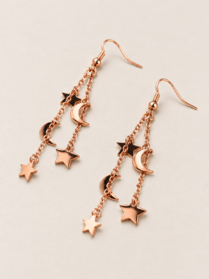 Rose Gold Moon and Star Chain Drop Earrings shown flat at an angle on a warm neutral background