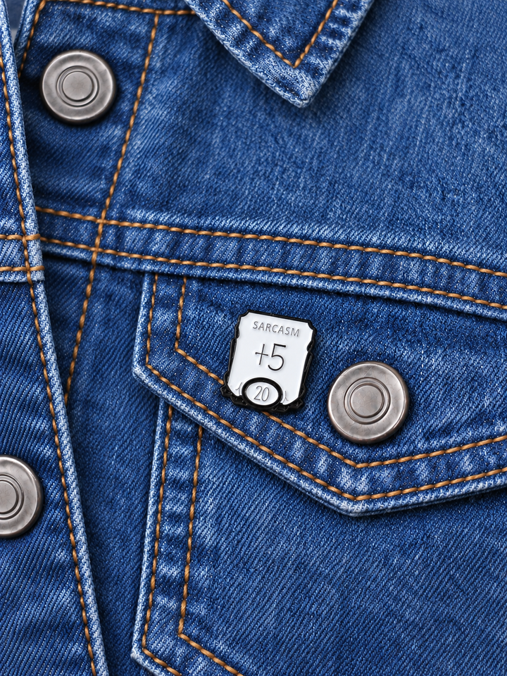 Sarcasm Plus Five D20 Pin displayed on a stonewash denim jacket beside a metal button
