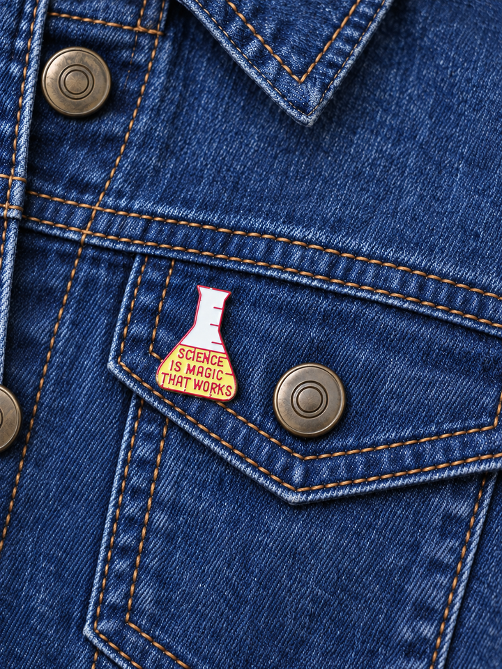 Science Is Magic That Works Flask Pin displayed on a dark indigo denim jacket beside a metal button