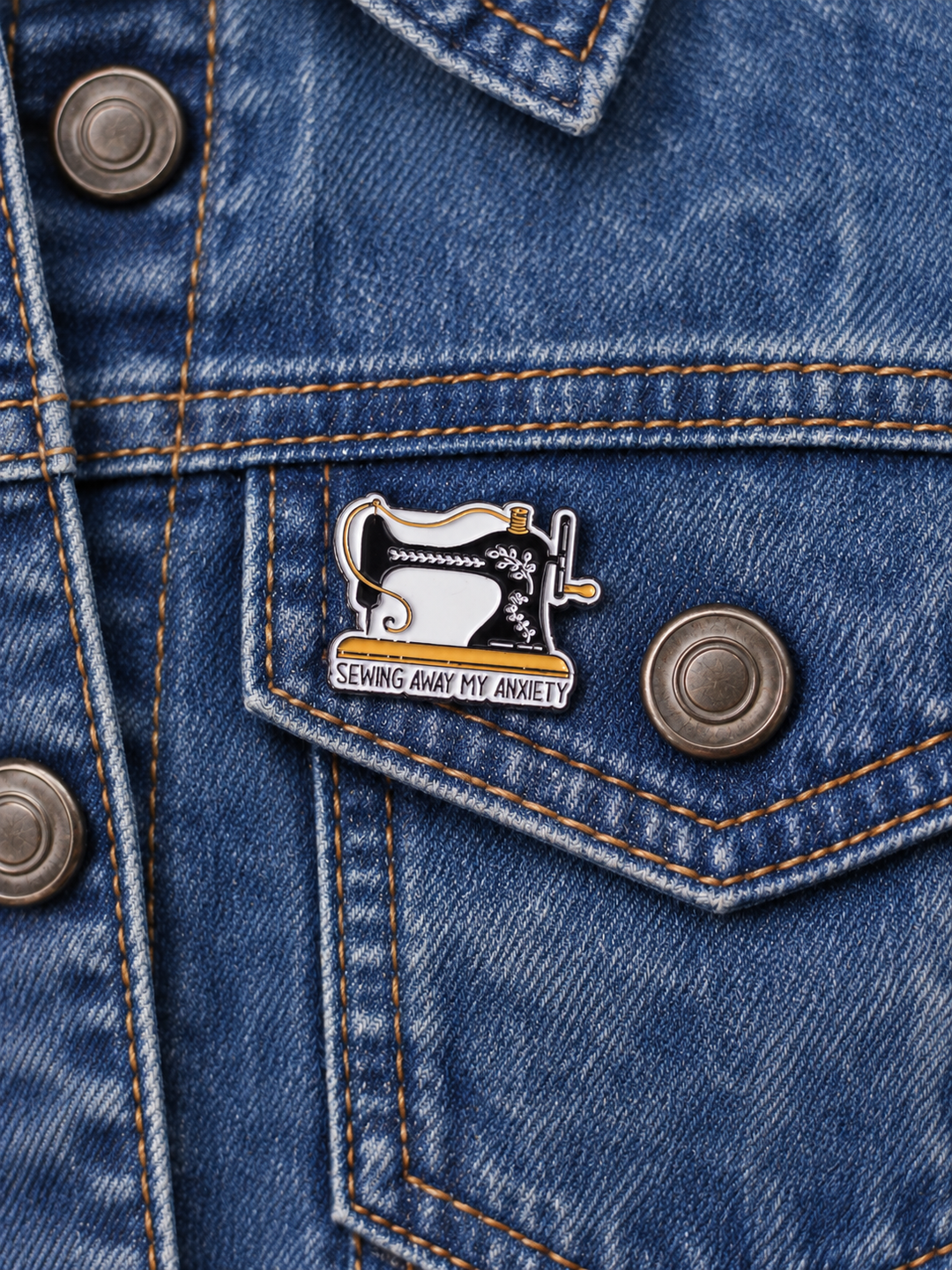 Sewing Away My Anxiety Sewing Machine Pin displayed on vintage faded denim beside a metal button