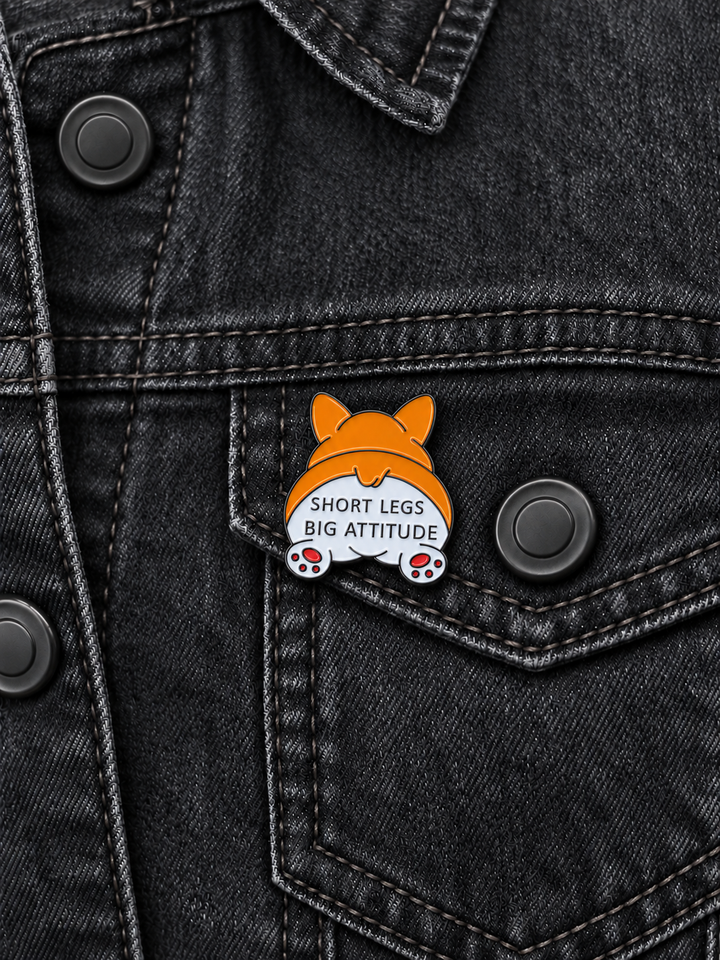 Short Legs Big Attitude Corgi Pin displayed on a black denim jacket beside a metal button