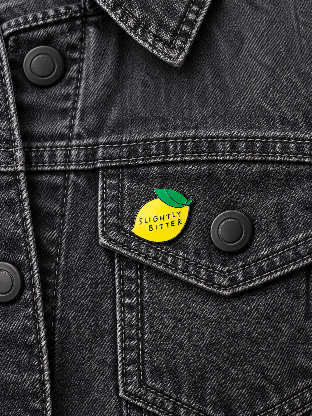 Slightly Bitter Pin displayed on a charcoal denim jacket beside a metal button