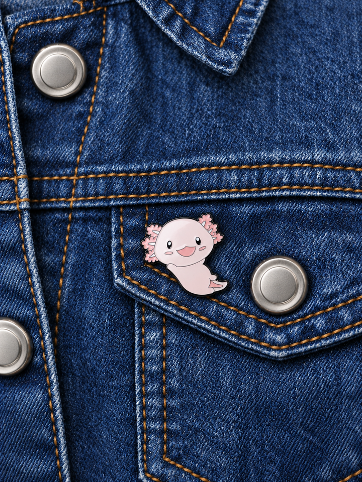 Smiling Pink Axolotl Pin displayed on dark indigo denim beside a metal button