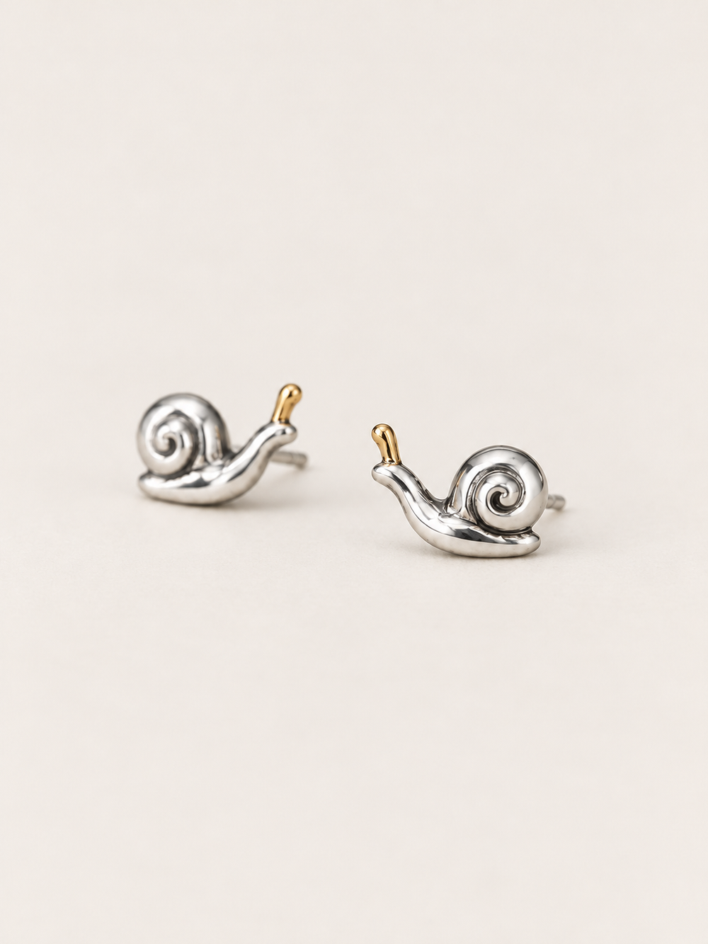 Snail Stud Earrings shown angled on a warm neutral background