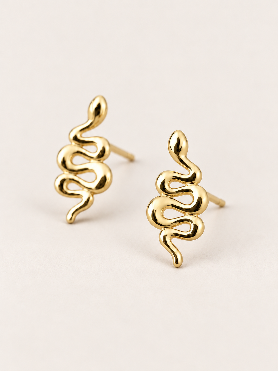 Gold Snake Stud Earrings shown angled on a warm neutral background