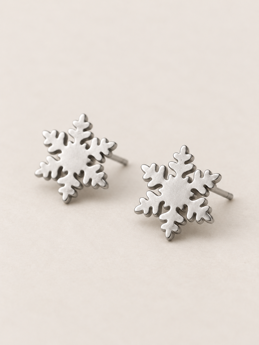 Silver Snowflake Stud Earrings shown angled on a warm neutral background
