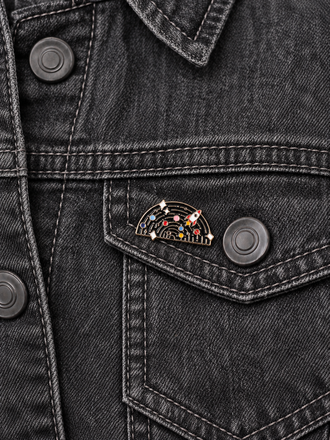 Solar System Rocket Pin displayed on a charcoal denim jacket beside a metal button