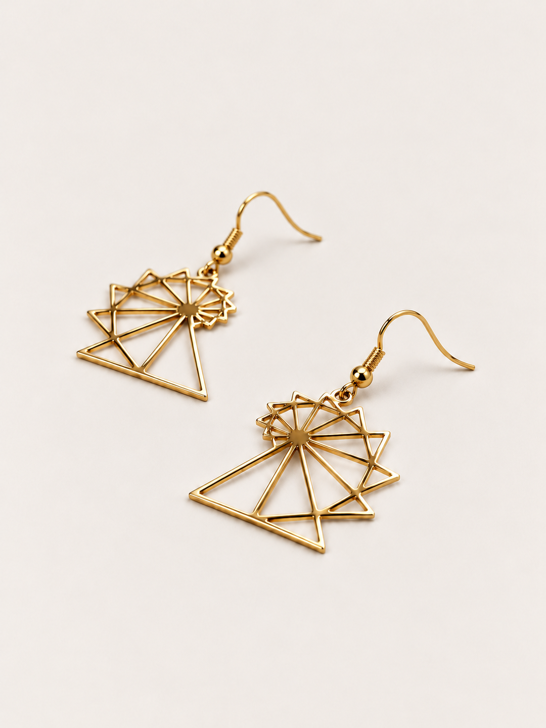Spiral of Theodorus Earrings in Gold lying flat at an angle on a warm neutral background