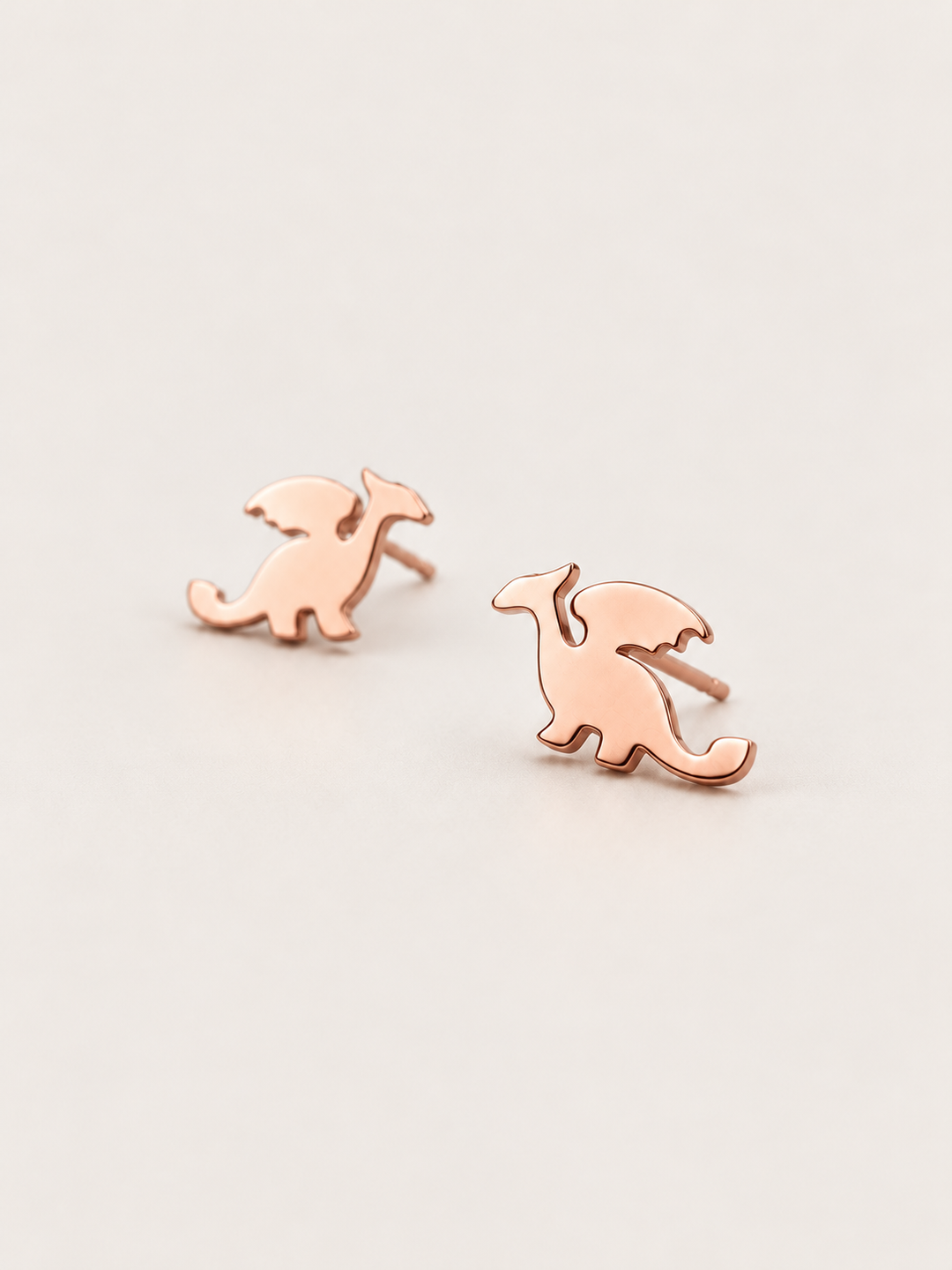 Rose Gold angled Stainless Steel Dragon Stud Earrings on a warm neutral background
