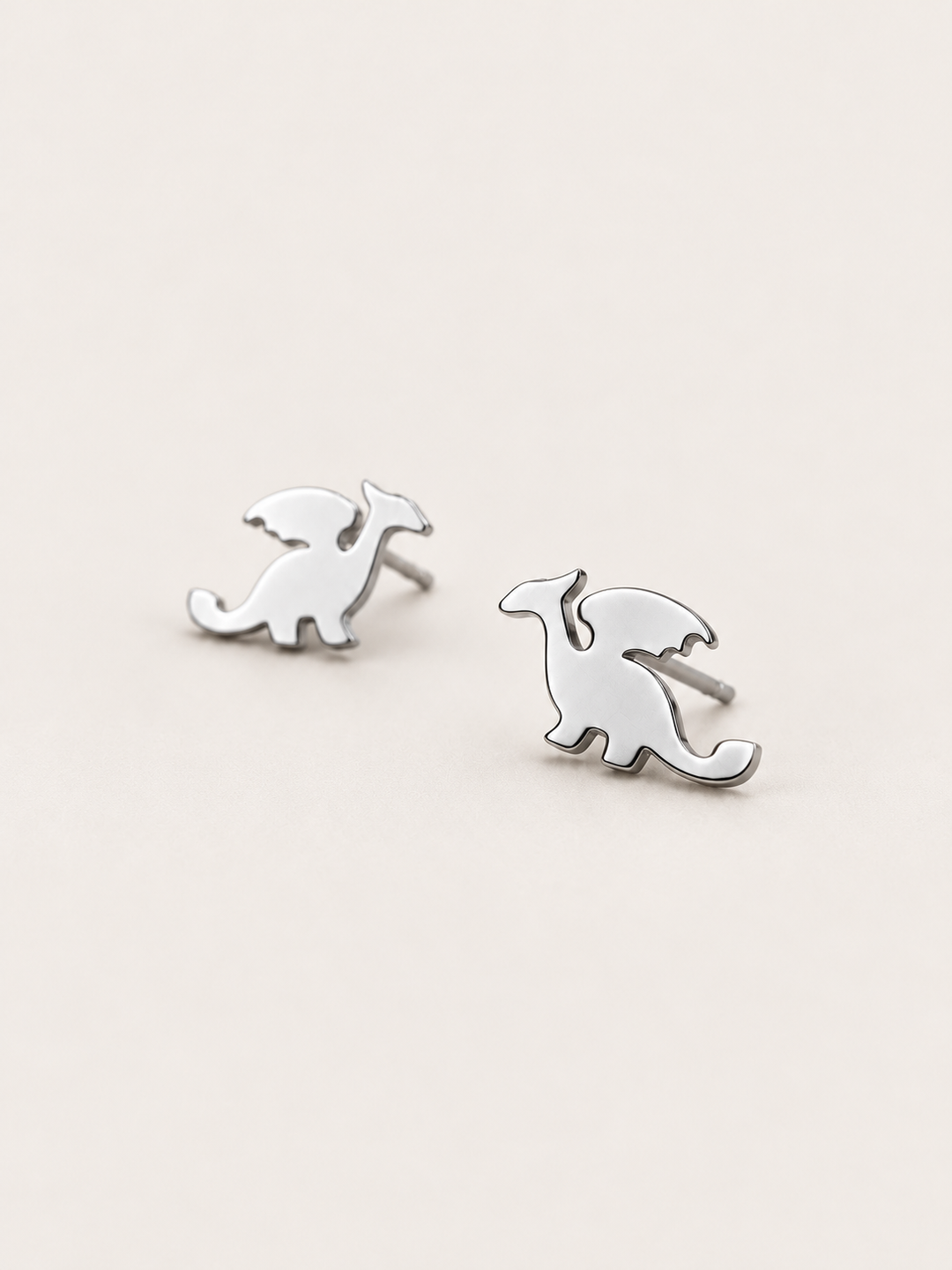 Silver angled Stainless Steel Dragon Stud Earrings on a warm neutral background