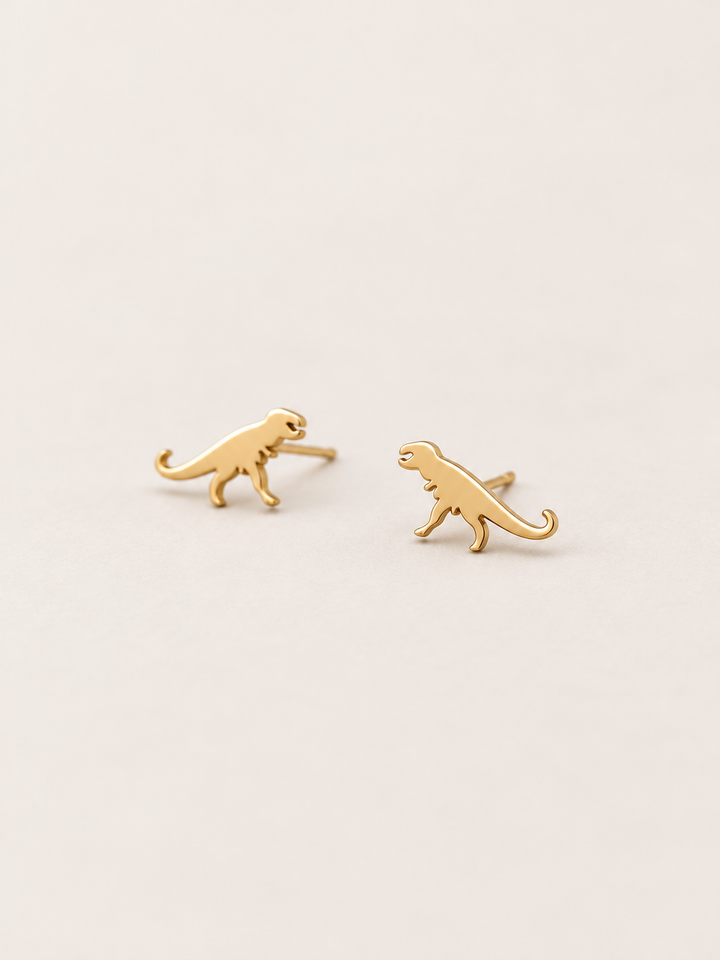 Gold T-Rex Dinosaur Stud Earrings shown angled on a warm neutral background