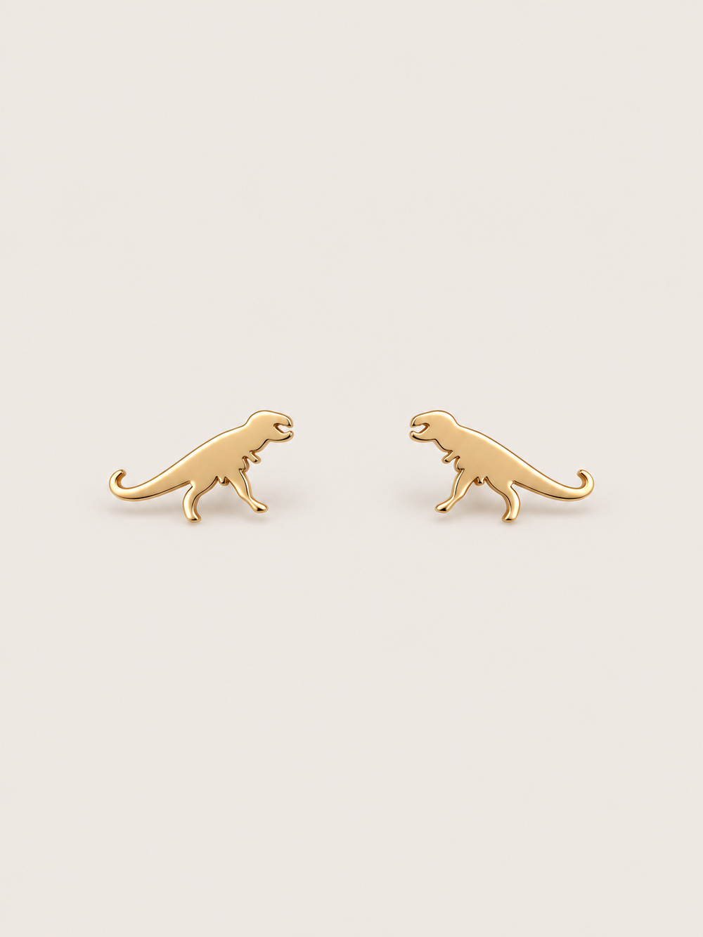 Gold T-Rex Dinosaur Stud Earrings shown on a warm neutral background