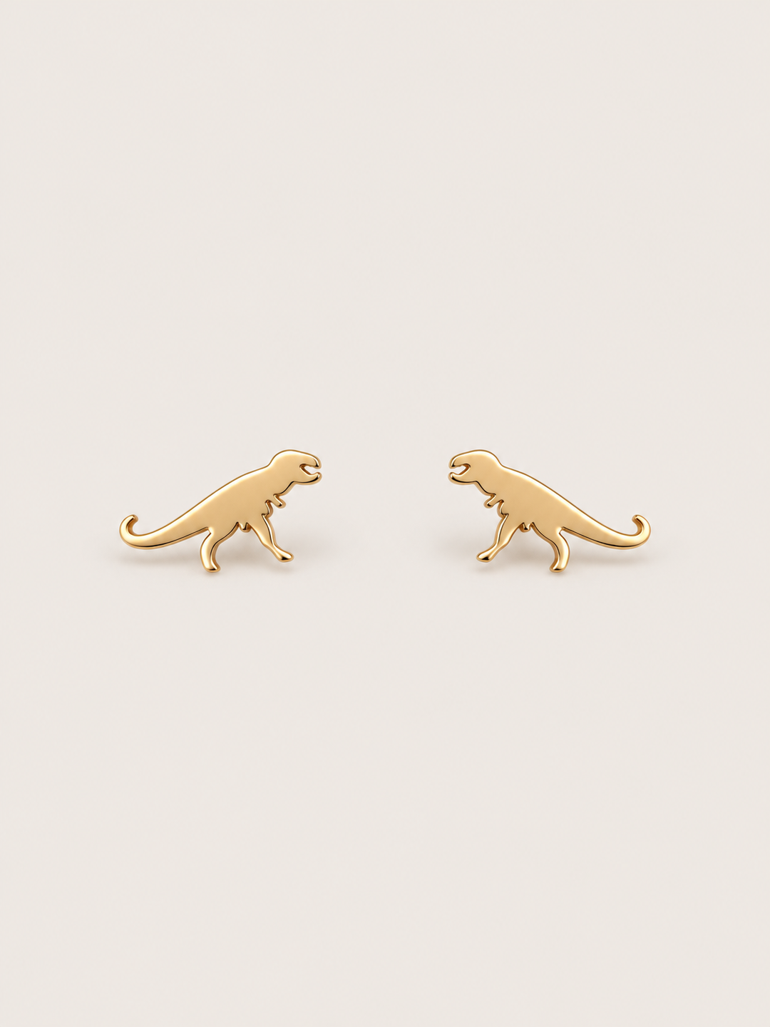 Gold T-Rex Dinosaur Stud Earrings shown on a warm neutral background