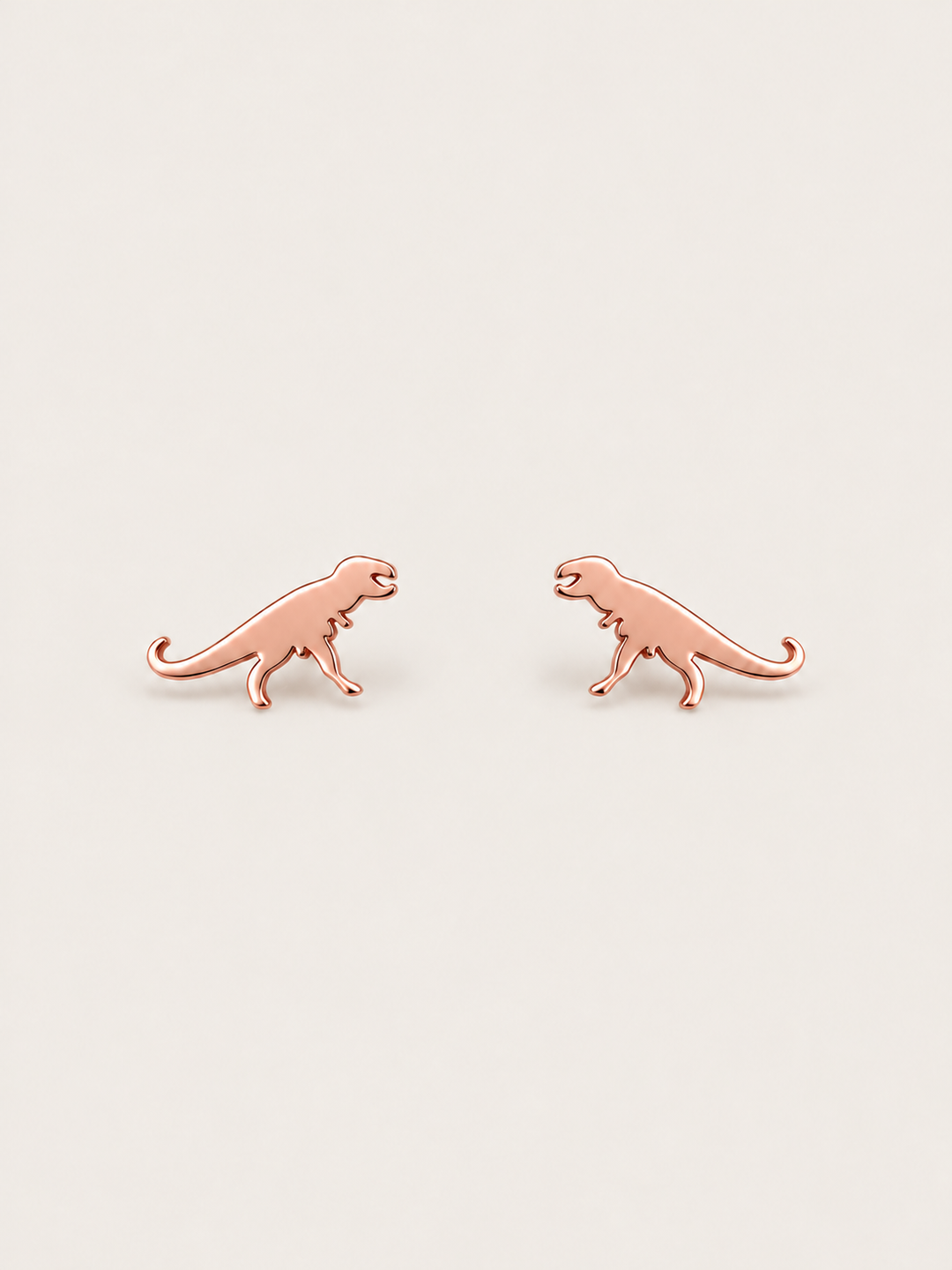 Rose Gold T-Rex Dinosaur Stud Earrings shown on a warm neutral background