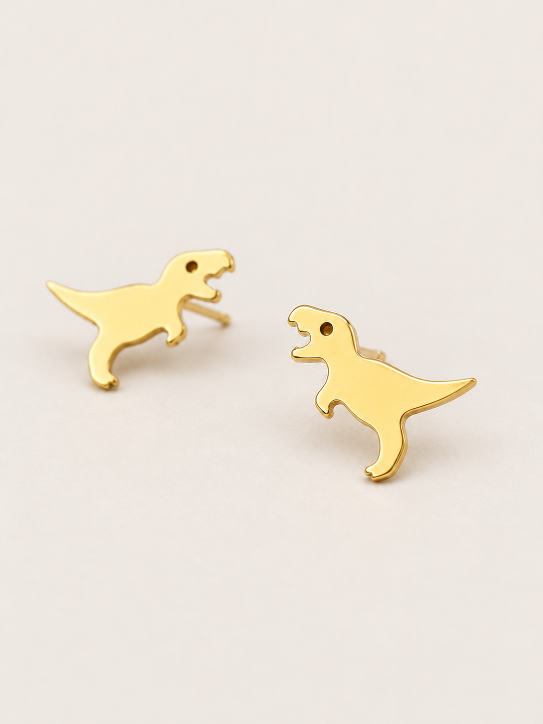 Gold T. Rex Stud Earrings shown angled on a warm neutral background
