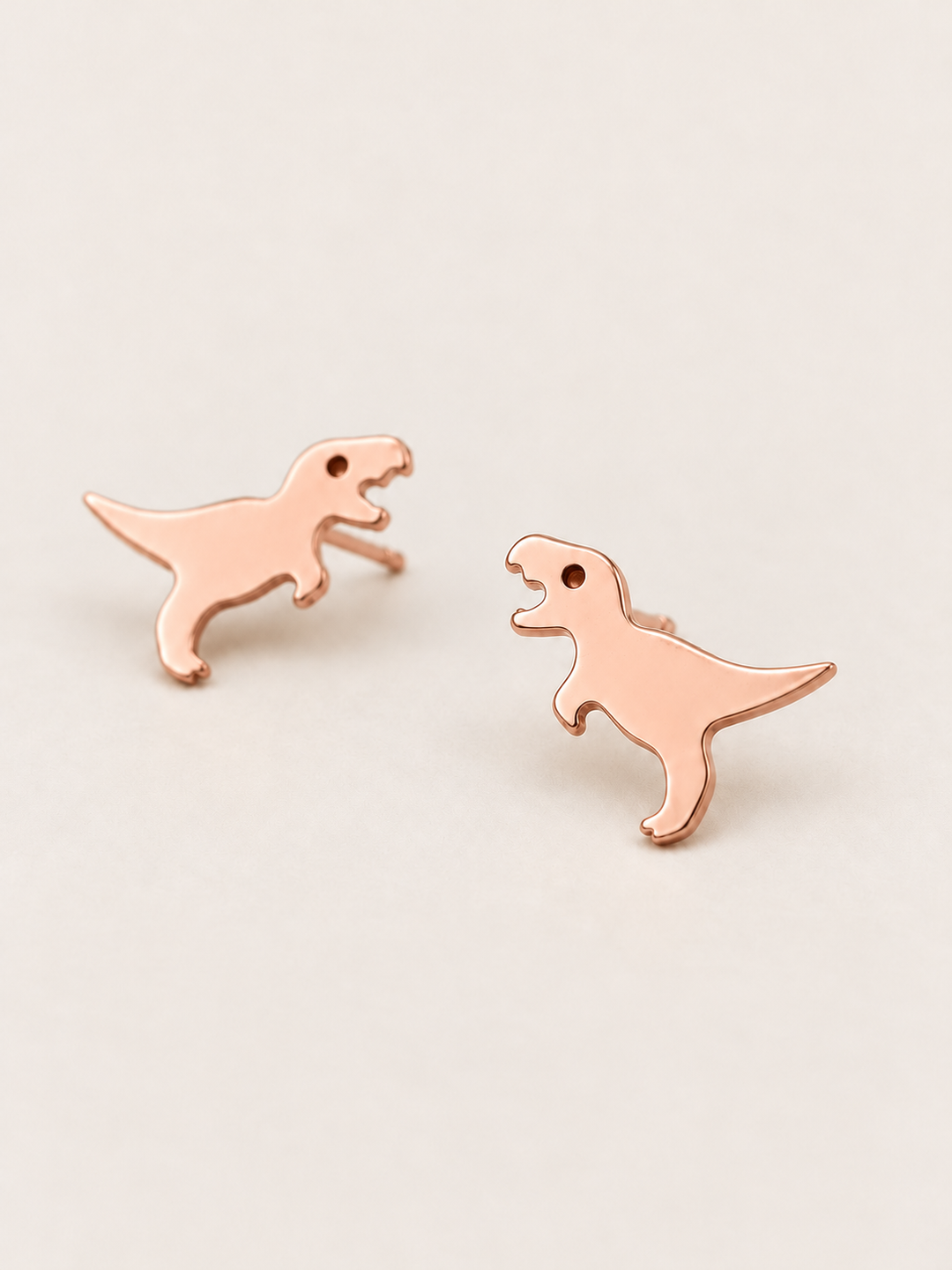 Rose Gold T. Rex Stud Earrings shown angled on a warm neutral background