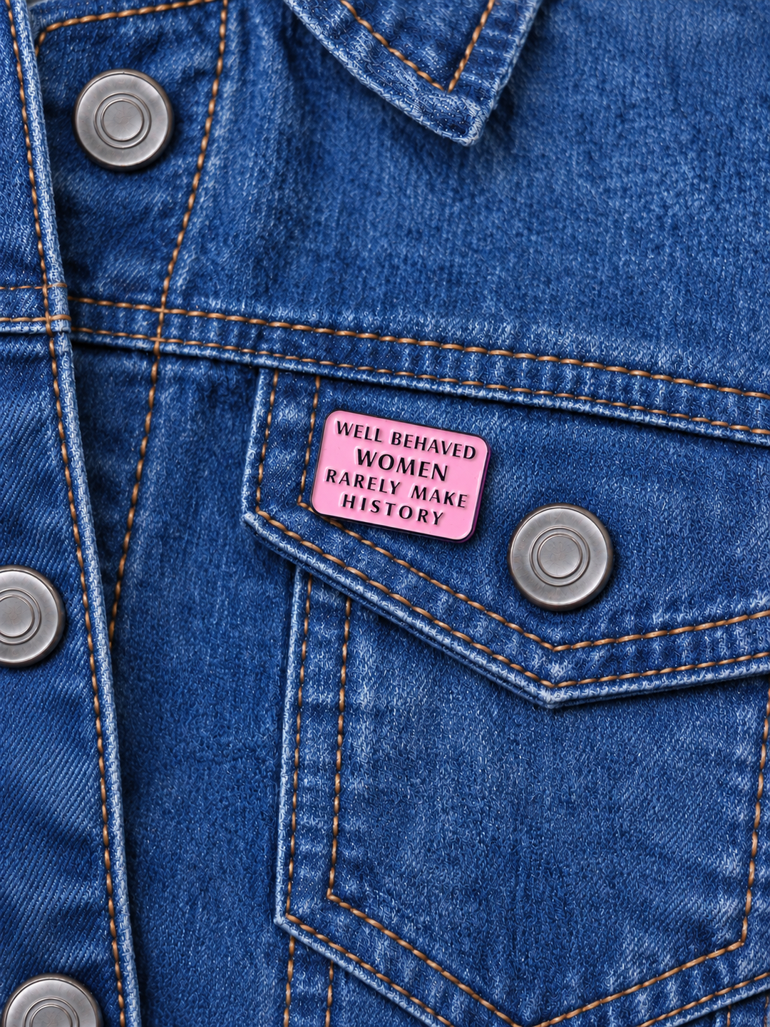 Well Behaved Women Rarely Make History Pin displayed on a stonewash denim jacket beside a metal button