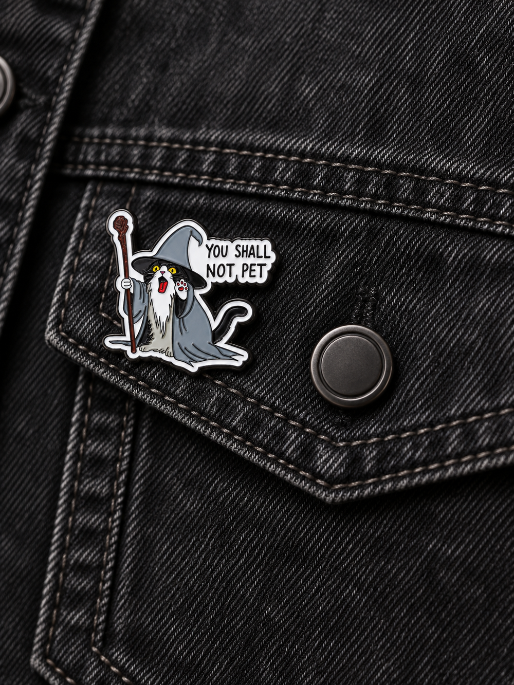 You Shall Not Pet Wizard Cat Pin displayed left of a centered button on a black denim pocket